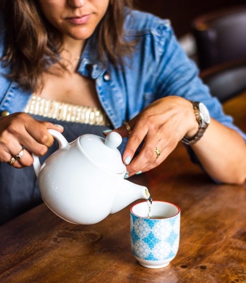 mulher serve chá em um pequeno copo de cerâmica