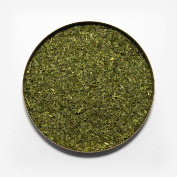 Imagem em fundo branco de uma tampa redonda com erva-mate pura folha dentro. Ervas com granulometria grossa e verde. Poucos palitos.