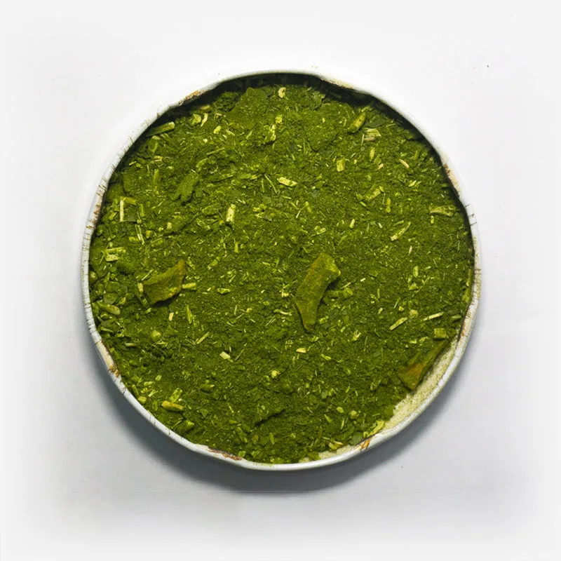 Erva-mate Composta Mate Nativo em recipiente metálico no centro. Fundo cinza claro. Erva-mate verde fresca. Pouca presença de palitos. Palitostriturados. Erva-mate padrão gaúcho composta de laranja e menta.