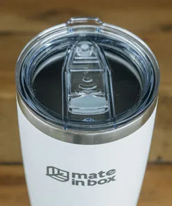 Copo Térmico em primeiro plano em cima de uma mesa de madeira. Foto mostra o copo em corpo inteiro, com tampa para bebidas quentes ou geladas. A tampa é abre fecha, facilitando assim viagens com borrachas de vedação. Tampa é em acrílico.